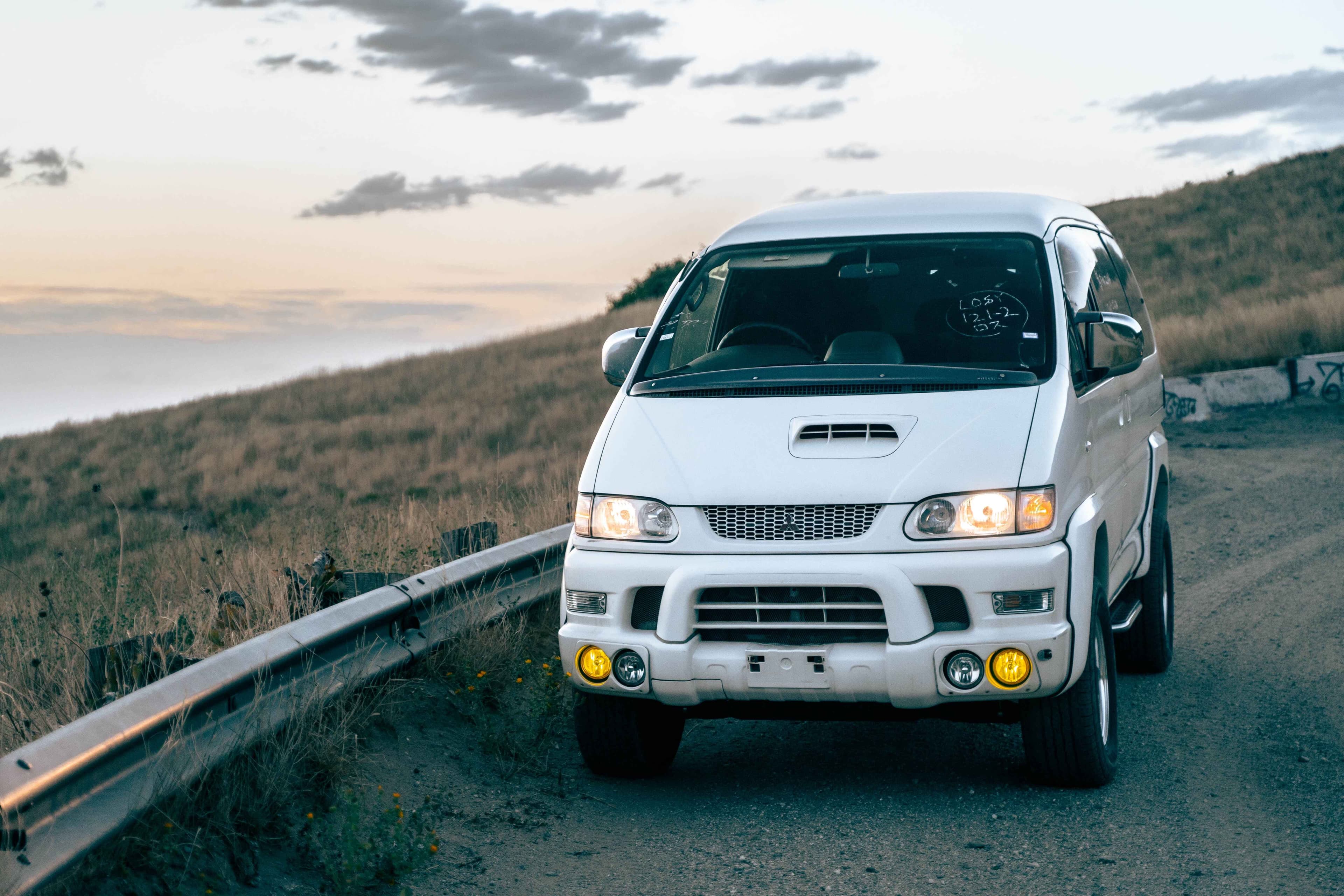 White Mitsubishi Delica Space Gear parked on a dirt road, facing camera.